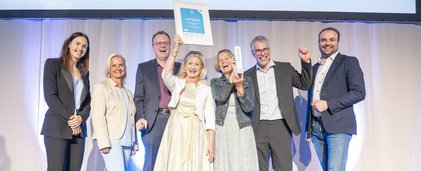 Gruppenbild mit sieben Personen. Dame in der Mitte hält Urkunde in die Höhe.